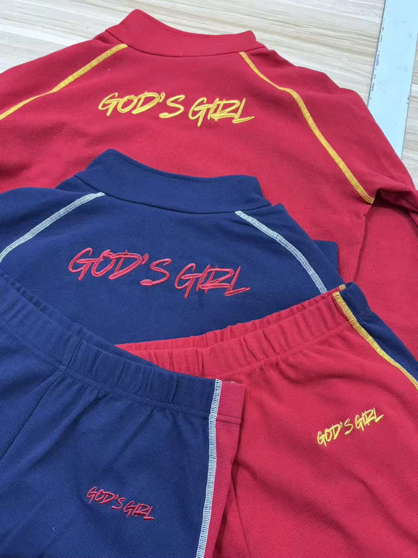 Red and blue shirts with 'GOD'S GIRL' text on a light wooden surface.