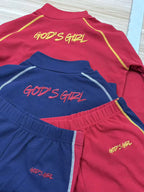 Red and blue shirts with 'GOD'S GIRL' text on a light wooden surface.
